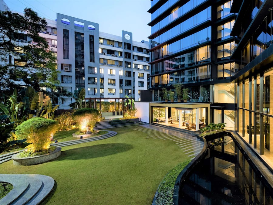 Un edificio moderno de varios pisos, con amplios ventanales y un patio bien cuidado, con zonas verdes y senderos.