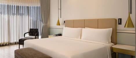 A modern hotel room with a large bed, a bedside table, a chair, and a desk.