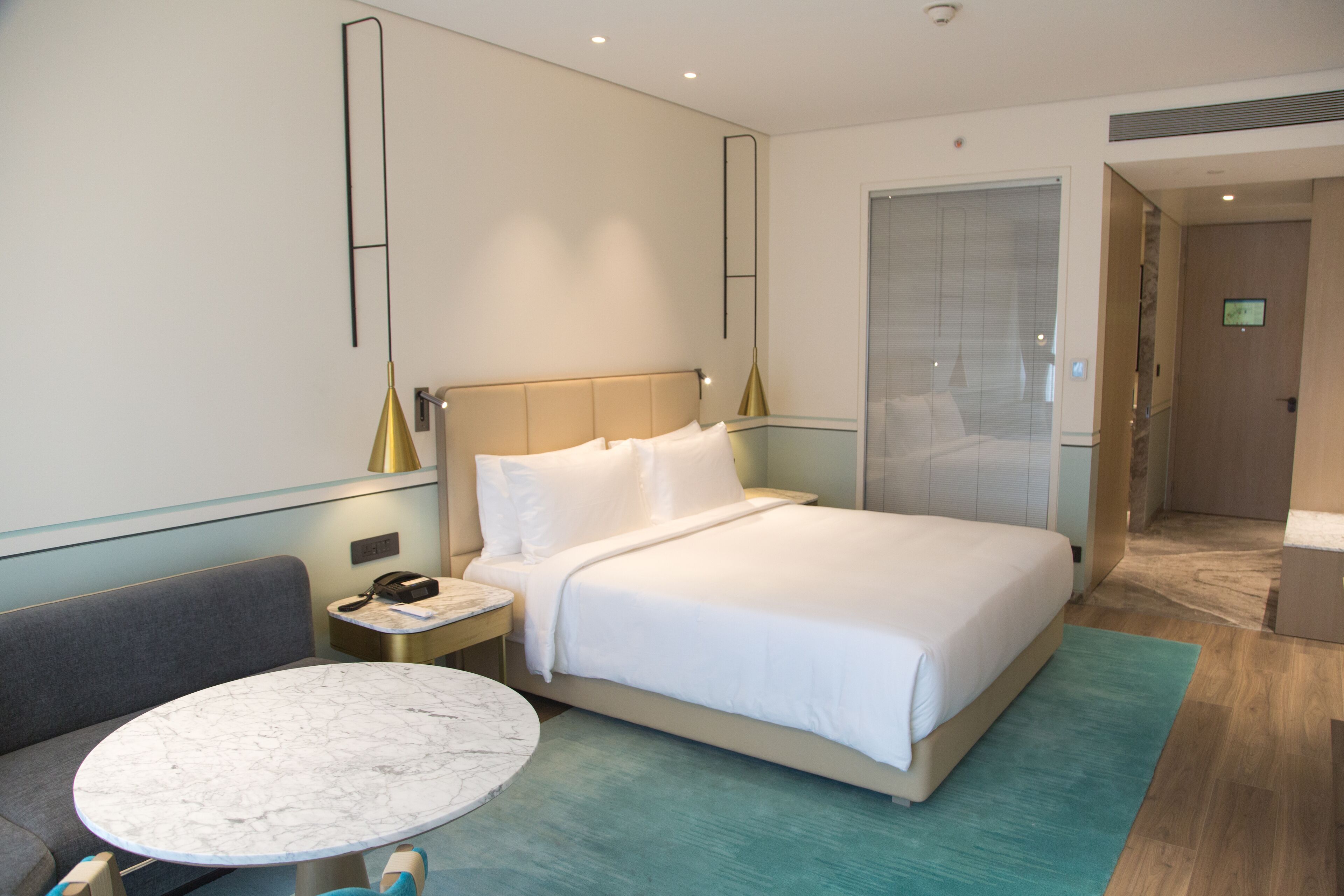 A modern hotel room with a large bed, a marble table, and a seating area.