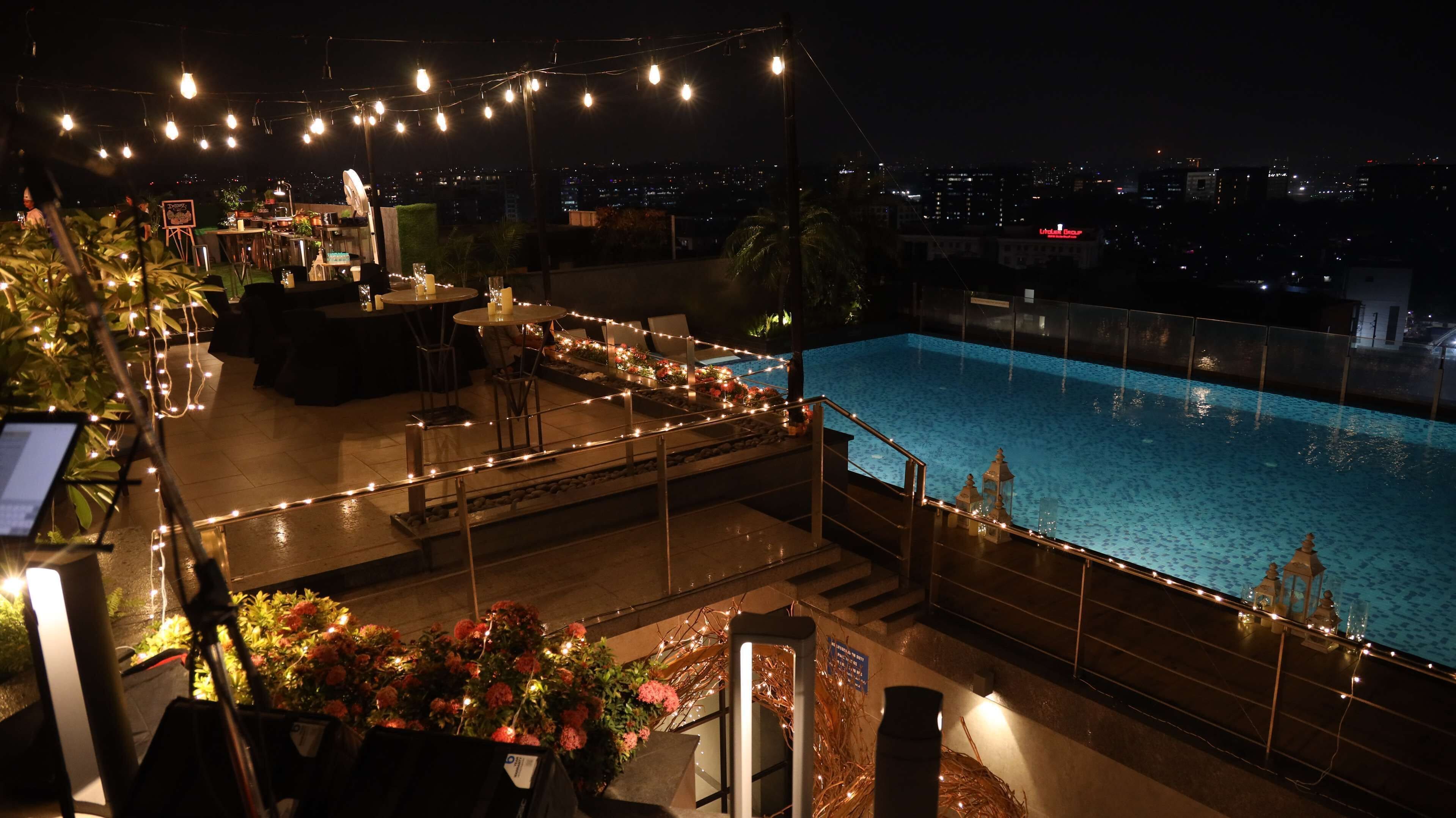 Ein Poolbereich im Freien mit Lichterketten, einer Bar und Blick auf die Stadt bei Nacht.