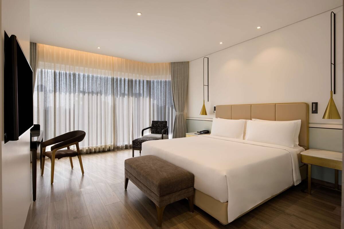A modern hotel room with a large bed, a desk, and a chair.