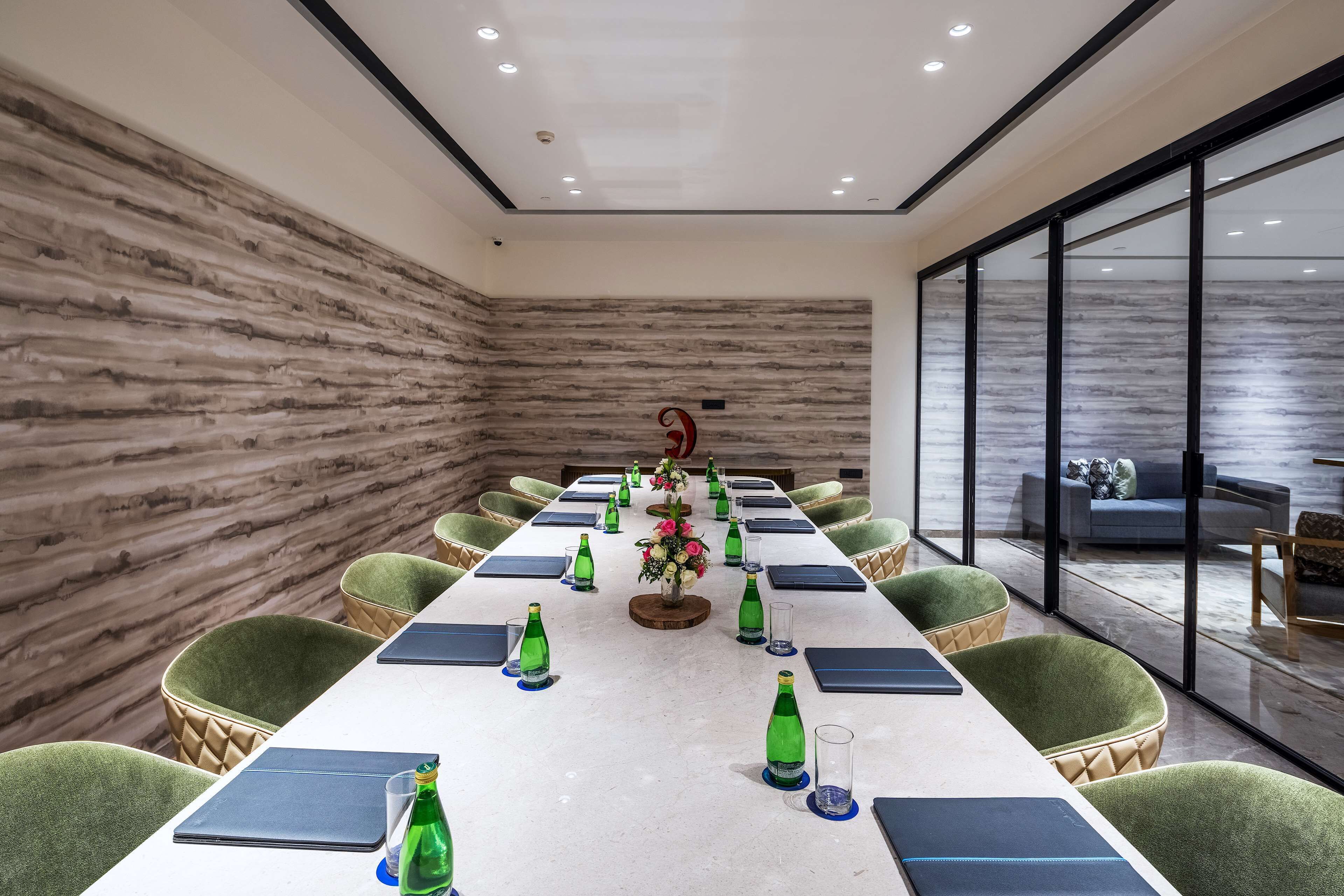 A conference room with a long table, green upholstered chairs, and a flower centerpiece.