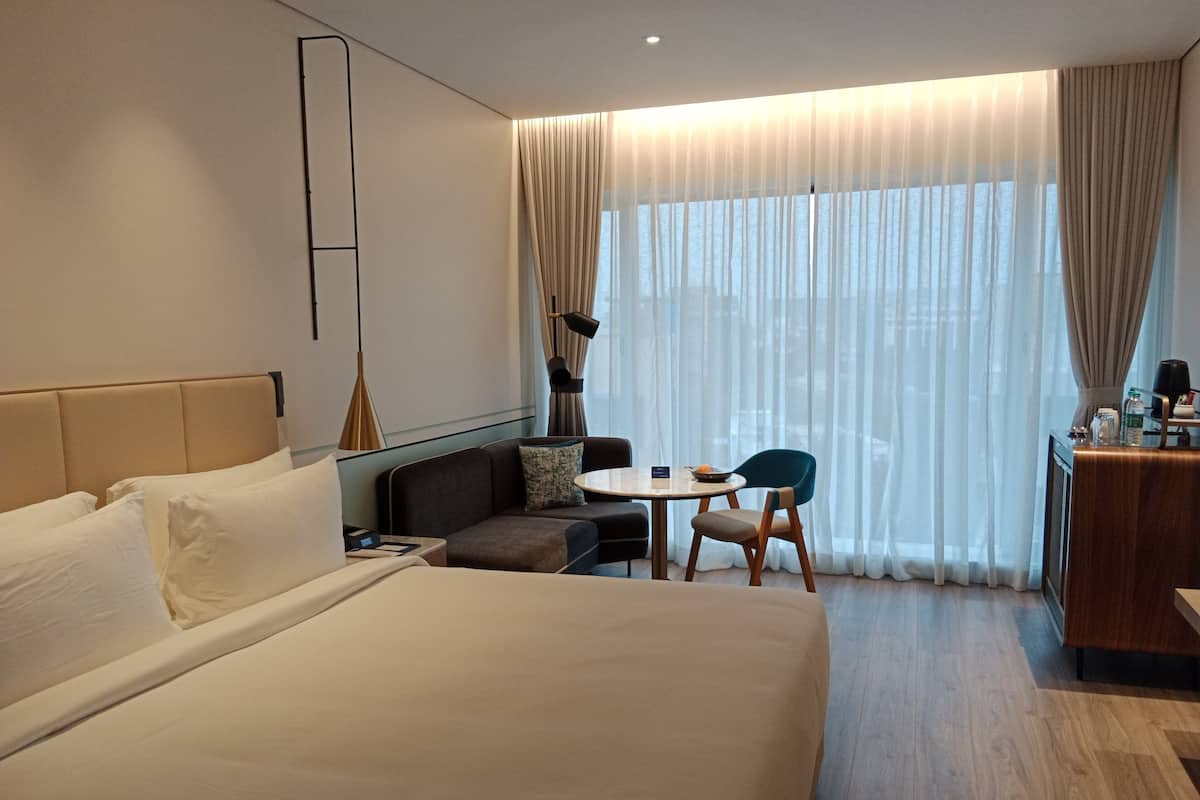 A hotel room with a large bed, a sofa, a small table with chairs, and a desk with a chair.