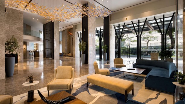 Een moderne lobby met een zithoek, grote ramen en een decoratief plafond.