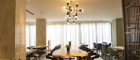 A conference room with a large oval table, multiple chairs, a chandelier, and a large window with curtains.
