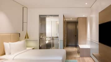 Une chambre d’hôtel moderne dotée d’un grand lit, d’une télévision et d’une salle de bain visible à travers une porte en verre.