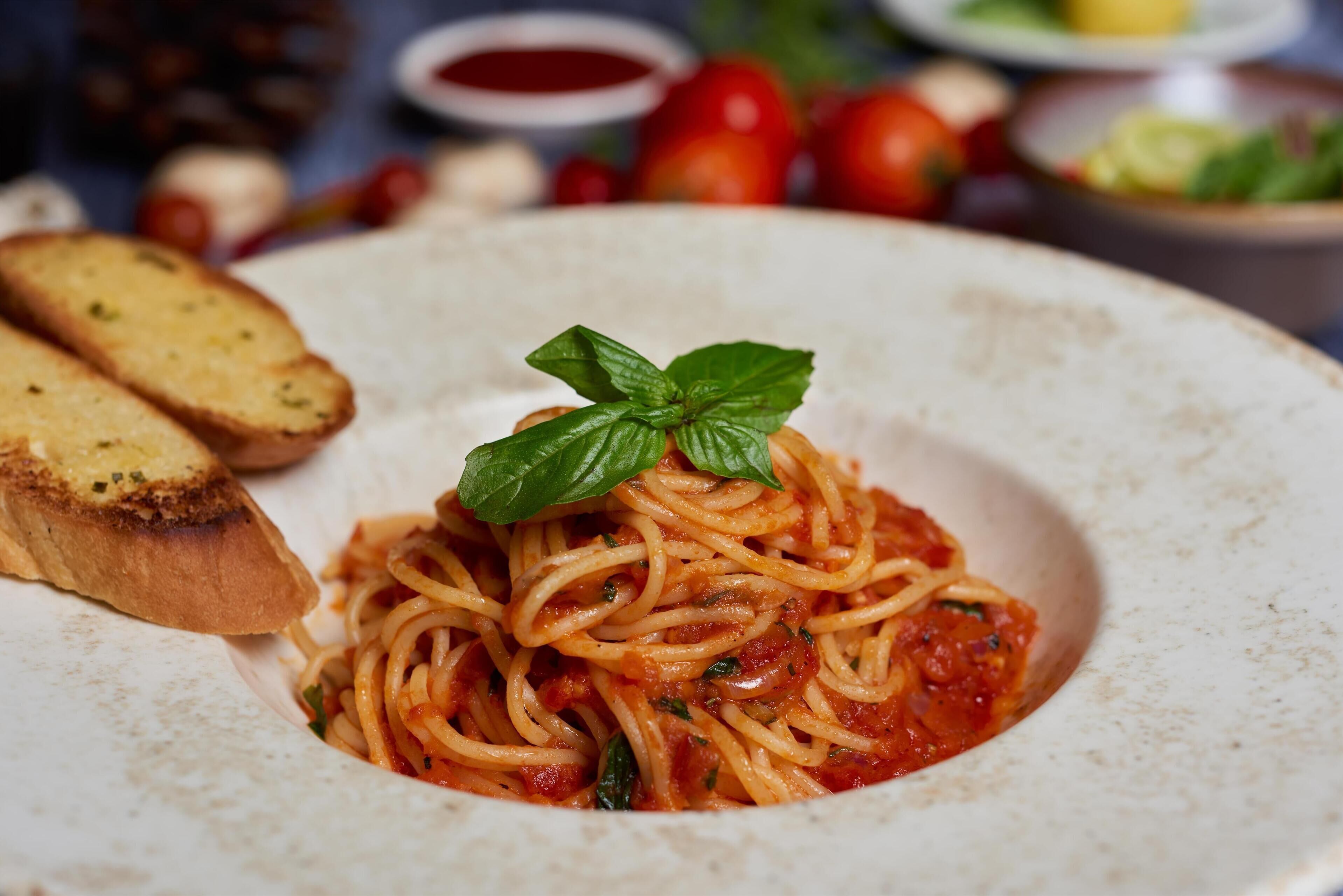 A plate of spaghetti with a basil leaf garnish, accompanied by toasted bread slices.