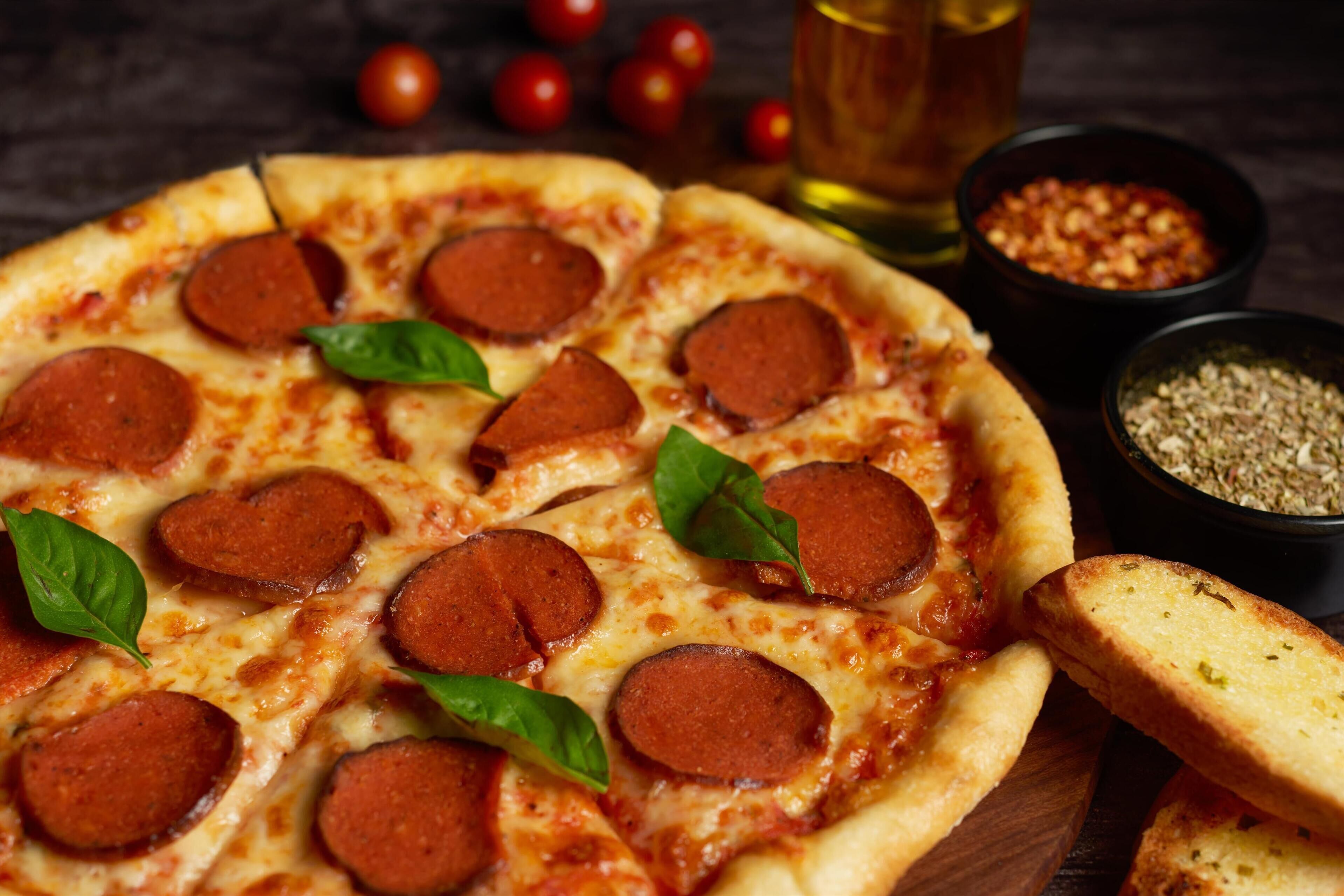 A pizza with pepperoni slices and basil leaves on a wooden board.