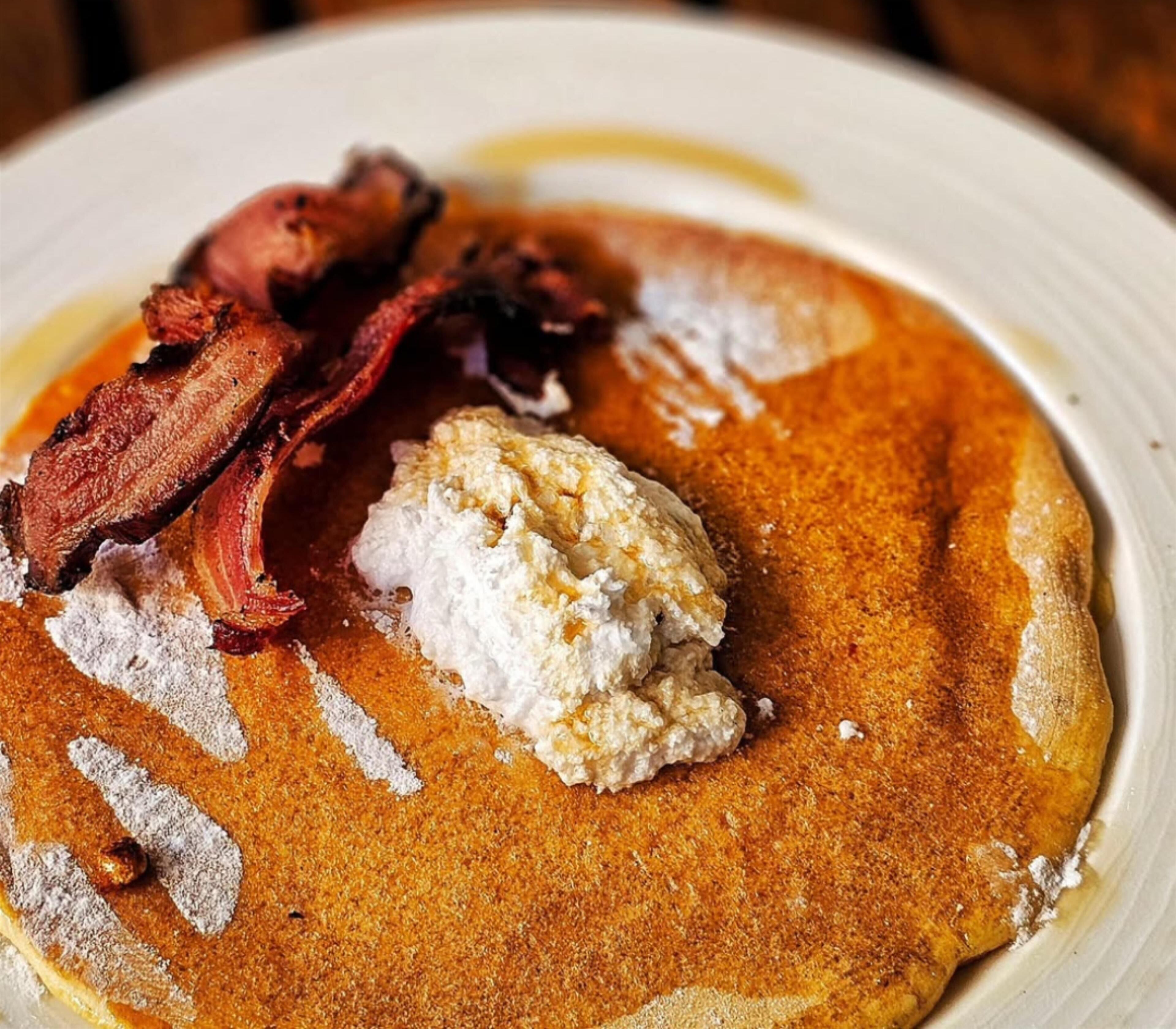 A plate with pancakes, bacon, and a dollop of cream.