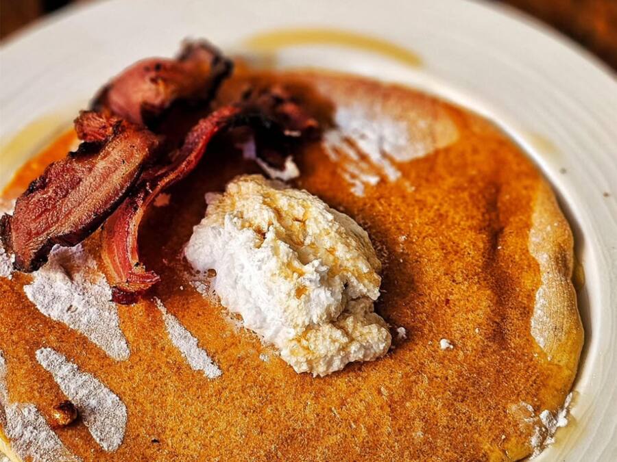 A plate with pancakes, bacon, and a dollop of cream.
