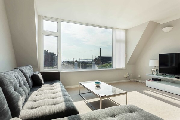 A modern living room with a large window, a sofa, a coffee table, and a TV stand.