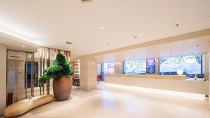 En rymlig entréhall med en receptionsdisk, en stor krukväxt och utsikt över omgivningarna genom stora fönster.