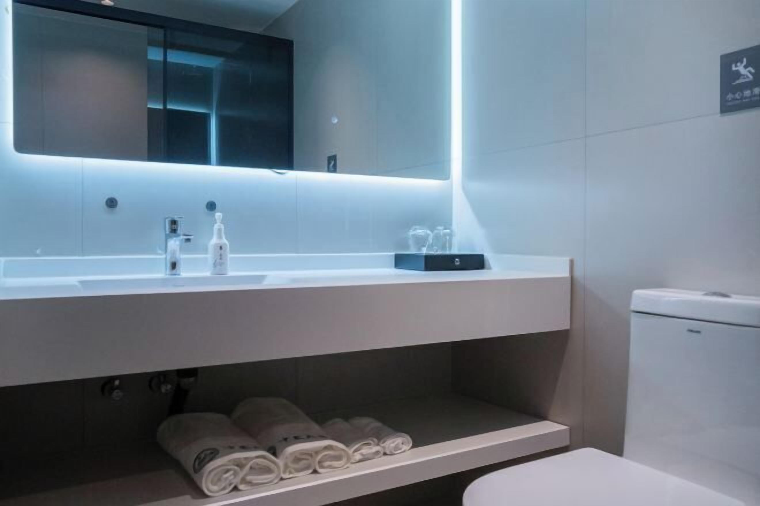 A modern bathroom with a large mirror, a sink, and a toilet. There are towels and toiletries on the counter.