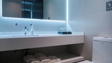 A modern bathroom with a large mirror, a sink, and a toilet. There are towels and toiletries on the counter.