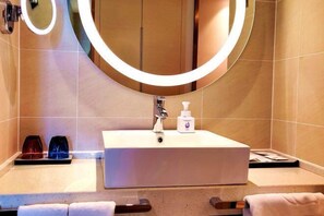 A bathroom with a white sink, a mirror with a light, and a bottle of hand soap.