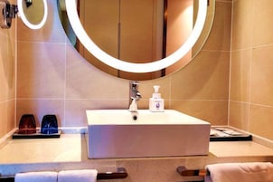 Un baño con un lavamanos blanco, un espejo con luz y una botella de jabón para manos.