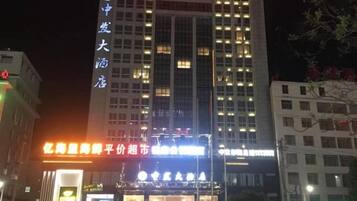 Un hotel de varios pisos con señalización iluminada, un cartel vertical llamativo a la izquierda y una entrada muy iluminada.