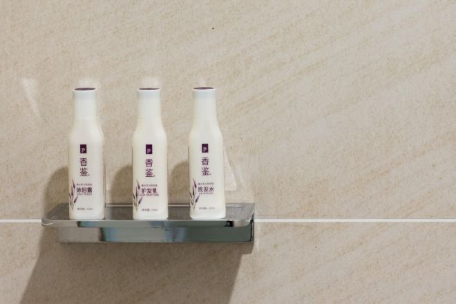 Three bottles of a product on a metallic shelf against a tiled wall.