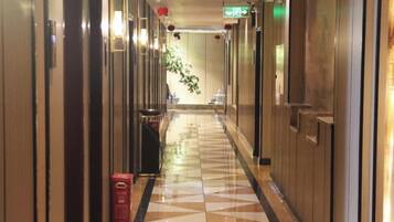 A hotel hallway with a patterned floor, doors on both sides, and a trash bin.