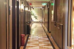 A hotel hallway with a patterned floor, doors on both sides, and a trash bin. - Zhongfa Hotel (Linxiang)