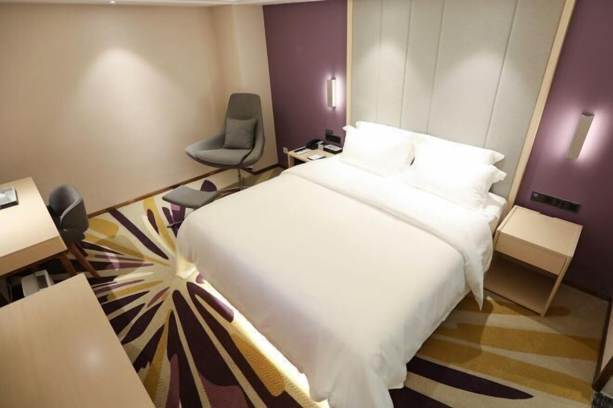 A hotel room with a large bed, a desk, a chair, and a nightstand.