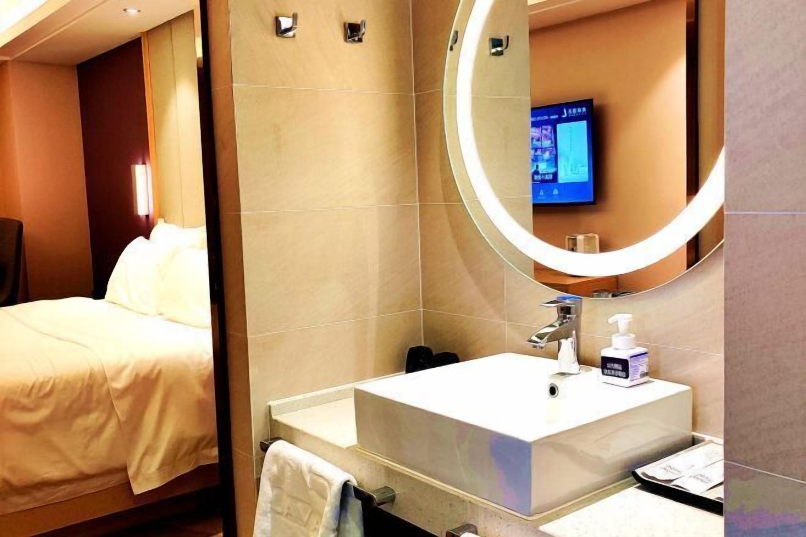 A hotel room with a bed, a large mirror, a sink, and a television mounted on the wall.