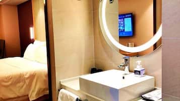 A hotel room with a bed, a large mirror, a sink, and a television mounted on the wall.