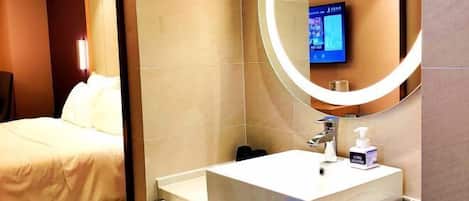 A hotel room with a bed, a large mirror, a sink, and a television mounted on the wall.