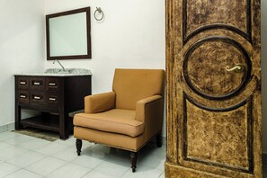 A room with a brown armchair, a dark wooden cabinet with drawers, a marble sink, and a large wooden door with a brass handle.