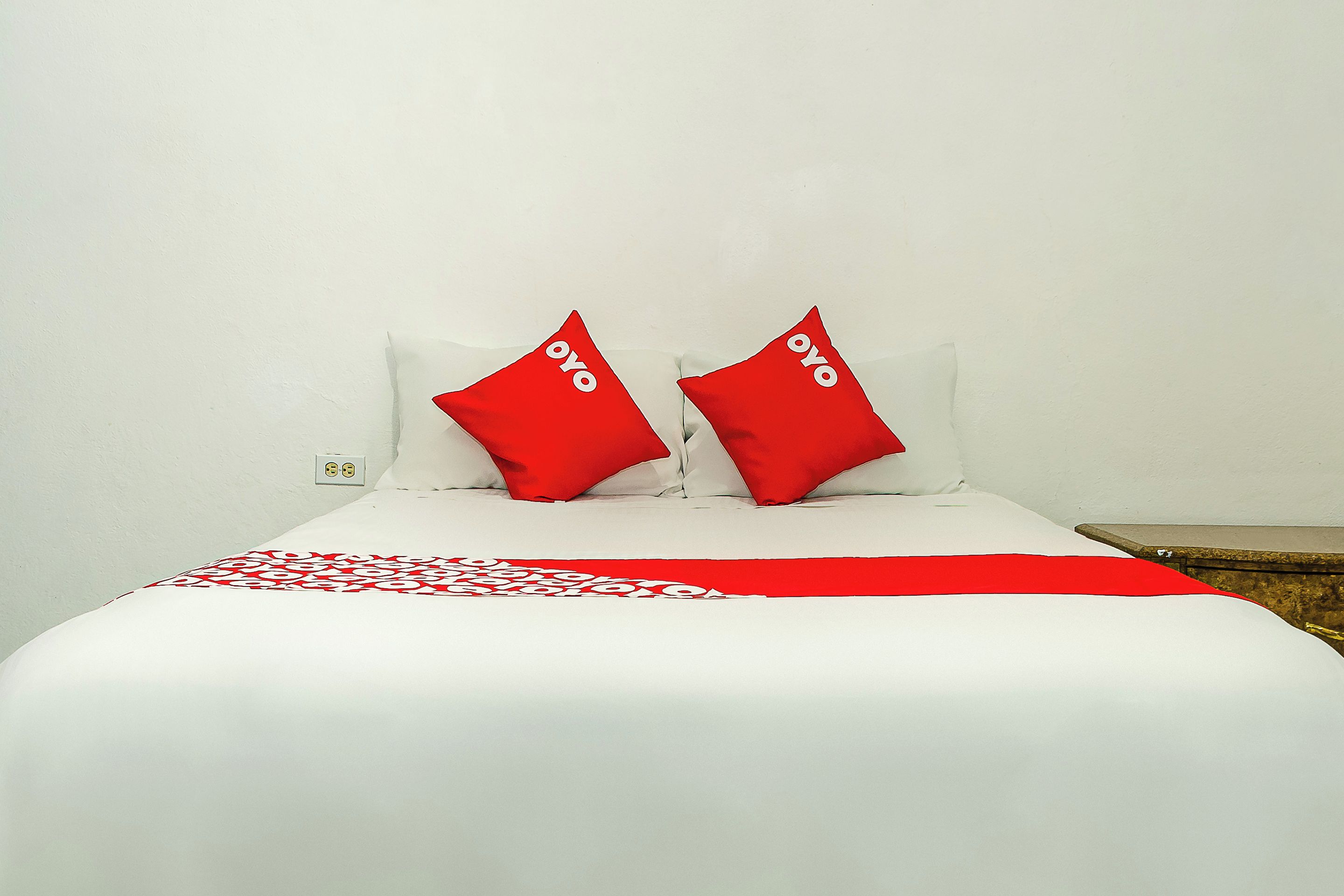 A bed with white bedding and two red pillows with the word "oyo" on them.