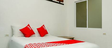 A neatly made bed with red and white bedding, a window with blinds, and a wall-mounted artwork above the bed.