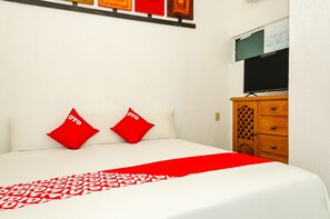A neatly made bed with a red and white patterned bedspread and two red pillows.