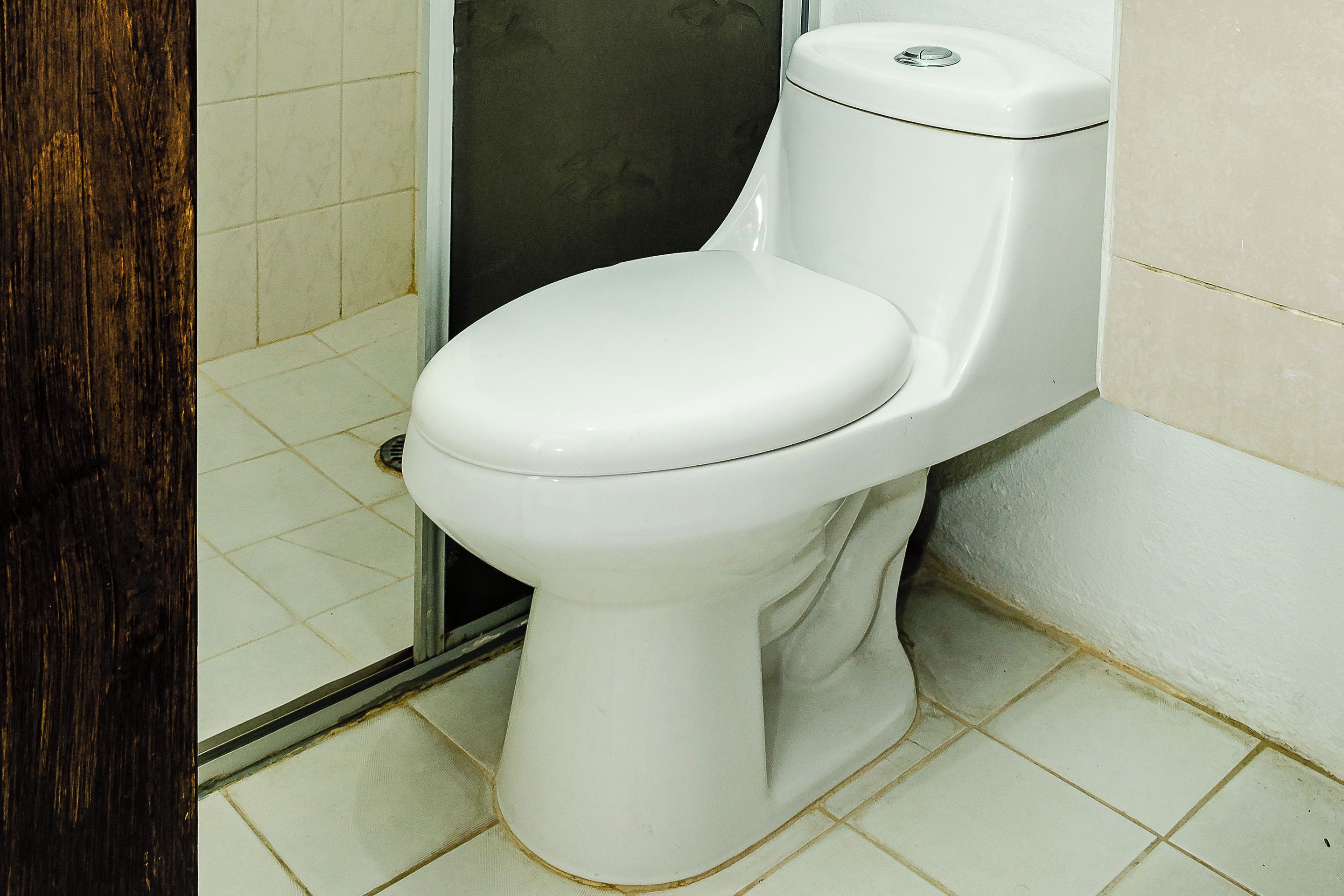 A white toilet in a bathroom with tiled flooring and a wooden door.