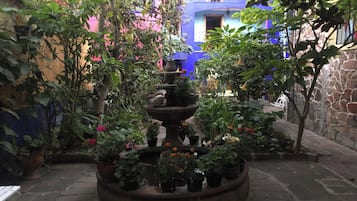 A courtyard with a central fountain surrounded by potted plants and a stone wall.