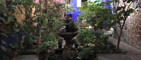 Een binnenplaats met een fontein in het midden, omringd door potplanten en een stenen muur.