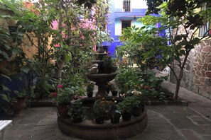 Un patio con una fuente central rodeada de plantas en macetas y un muro de piedra.
