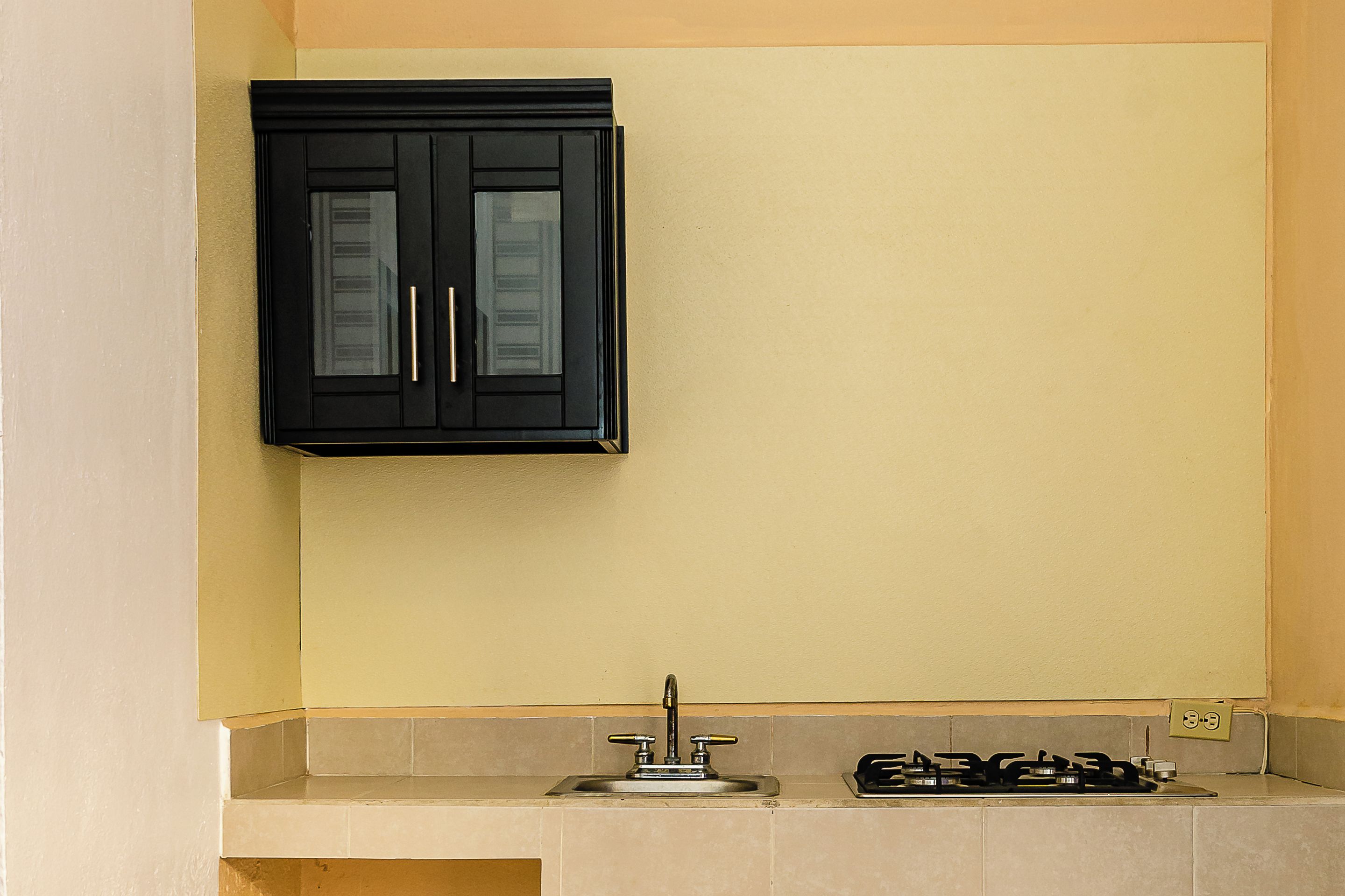 Una cocina con un gabinete negro sobre una encimera color crema, un lavamanos y una estufa a gas.