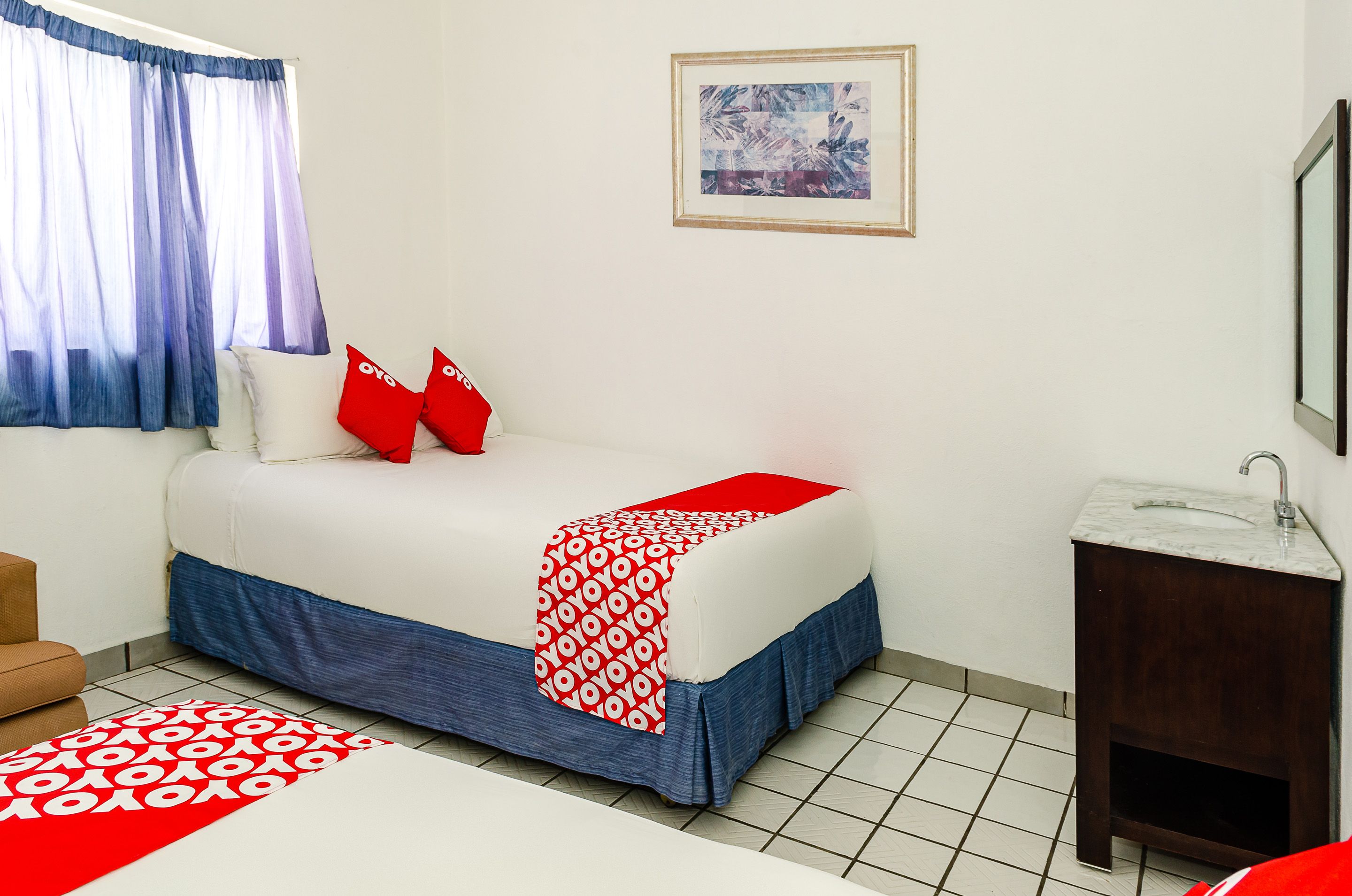 Una habitación de hotel con cama, baño pequeño y ventana con cortinas.