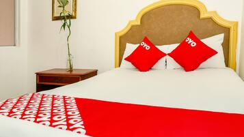 A neatly made bed with a red and white bedspread, two red pillows with the word "oyo" on them, and a wooden nightstand with a vase of flowers.
