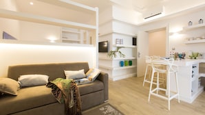 A modern living room with a sofa, a coffee table, and a kitchen area with white bar stools. - Palermoinsuite Aparthotel (Palermo)