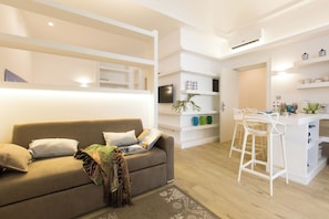 A modern living room with a sofa, a coffee table, and a kitchen area with white bar stools. - Palermoinsuite Aparthotel (Palermo)