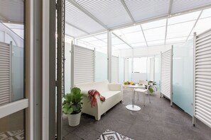 A modern, open-plan living area with a white sofa, a small round table with a lamp, and a potted plant. - Palermoinsuite Aparthotel (Palermo)
