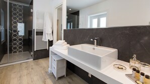 Ein modernes Badezimmer mit einem großen weißen Waschbecken, dunklen Marmorwänden und einer Duschkabine aus Glas.