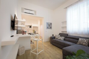A modern living room with a grey sofa, a white coffee table, and a dining area with a white chair and a small table. - Palermoinsuite Aparthotel (Palermo)