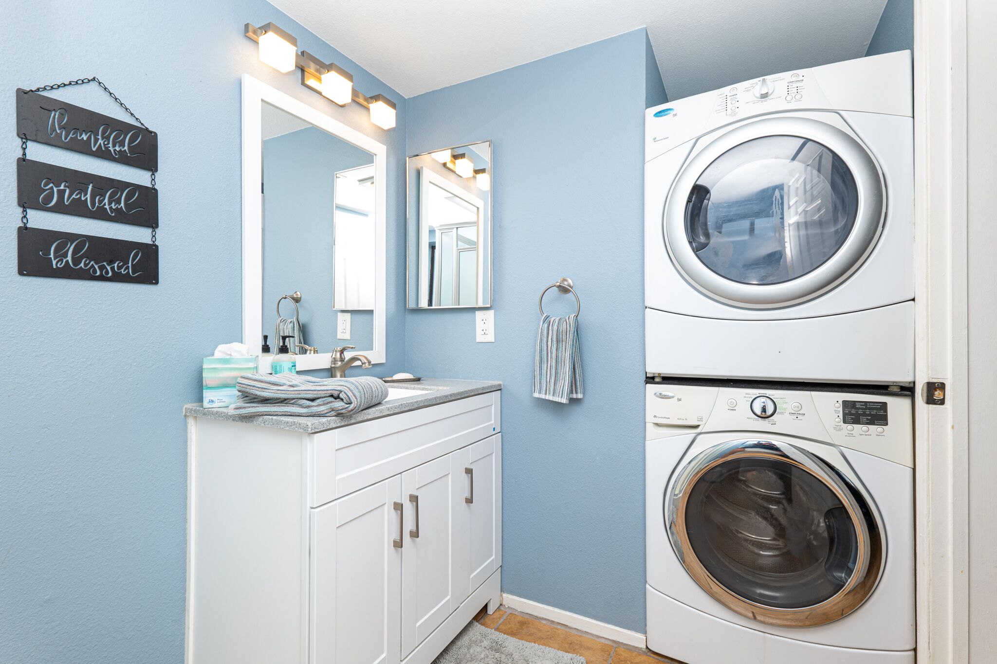 Un espace buanderie comprenant un lave-linge, un évier avec un miroir et un porte-serviettes.