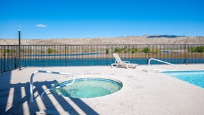 An outdoor swimming pool with lounge chairs, a hot tub, and a view of a desert landscape.