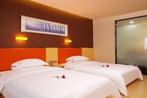 A hotel room with two beds, each with white bedding and a red rose on the bed. There is a painting on the wall above the beds and a glass partition on the right side.