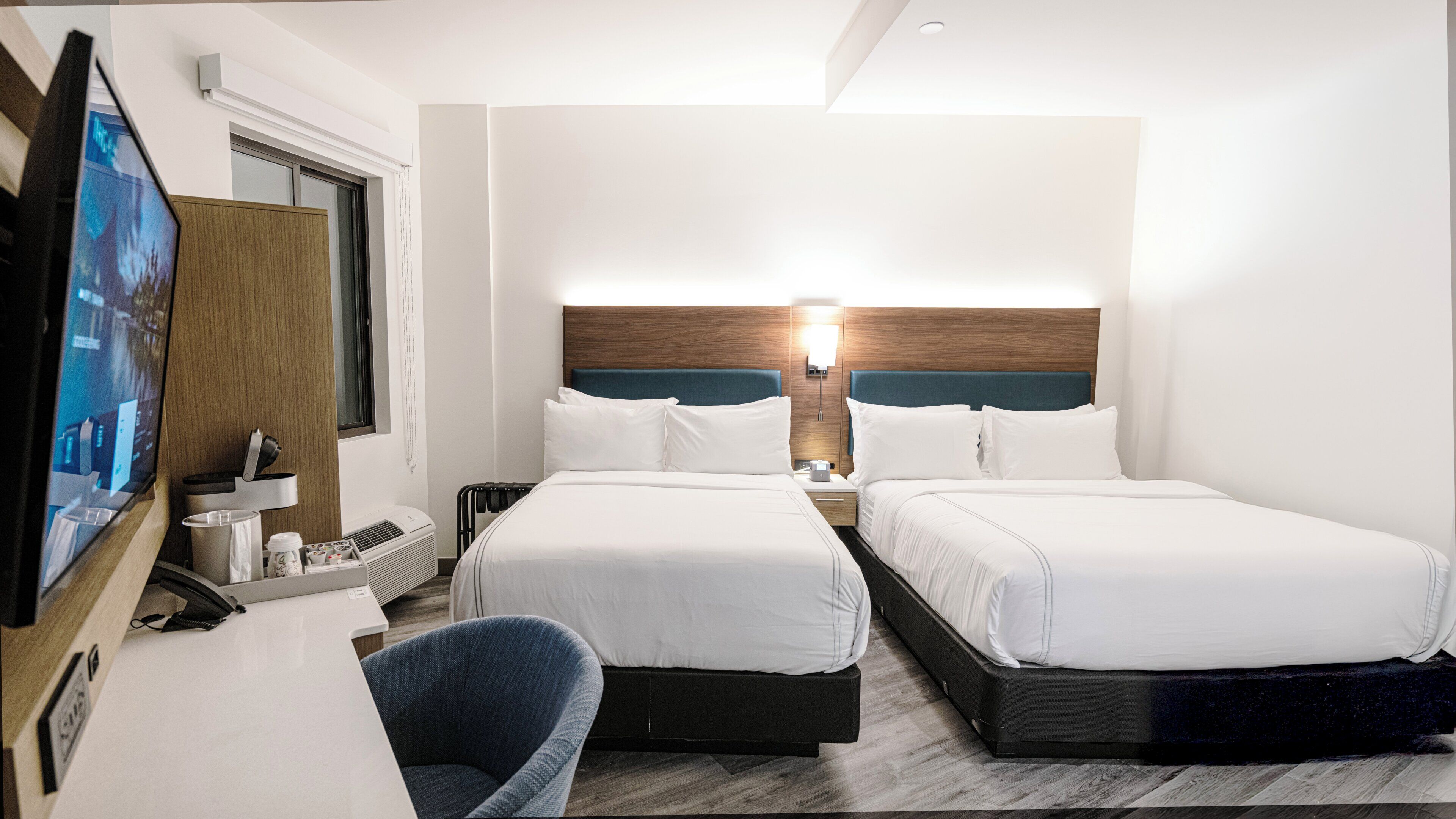 A hotel room with two beds, a desk with a computer, a chair, and a TV.