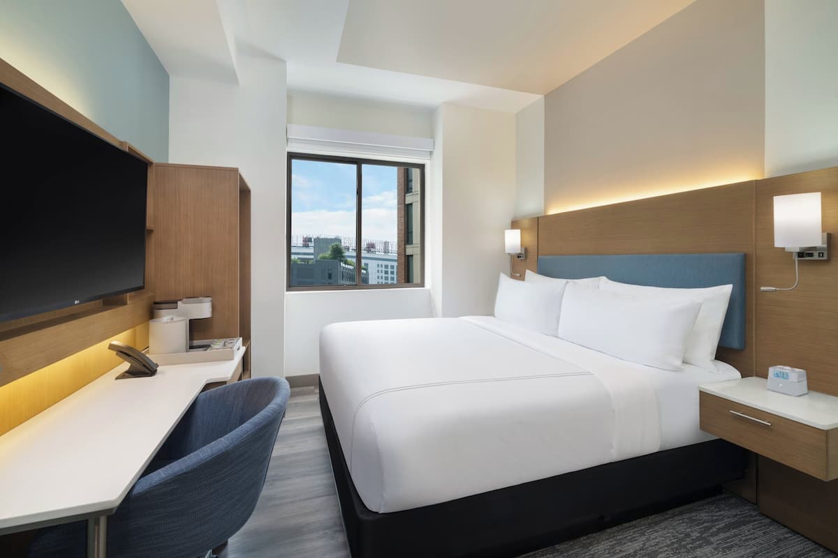 Une chambre d’hôtel équipée d’un lit, d’un bureau, d’une chaise, d’une télévision et d’une fenêtre donnant sur la ville.