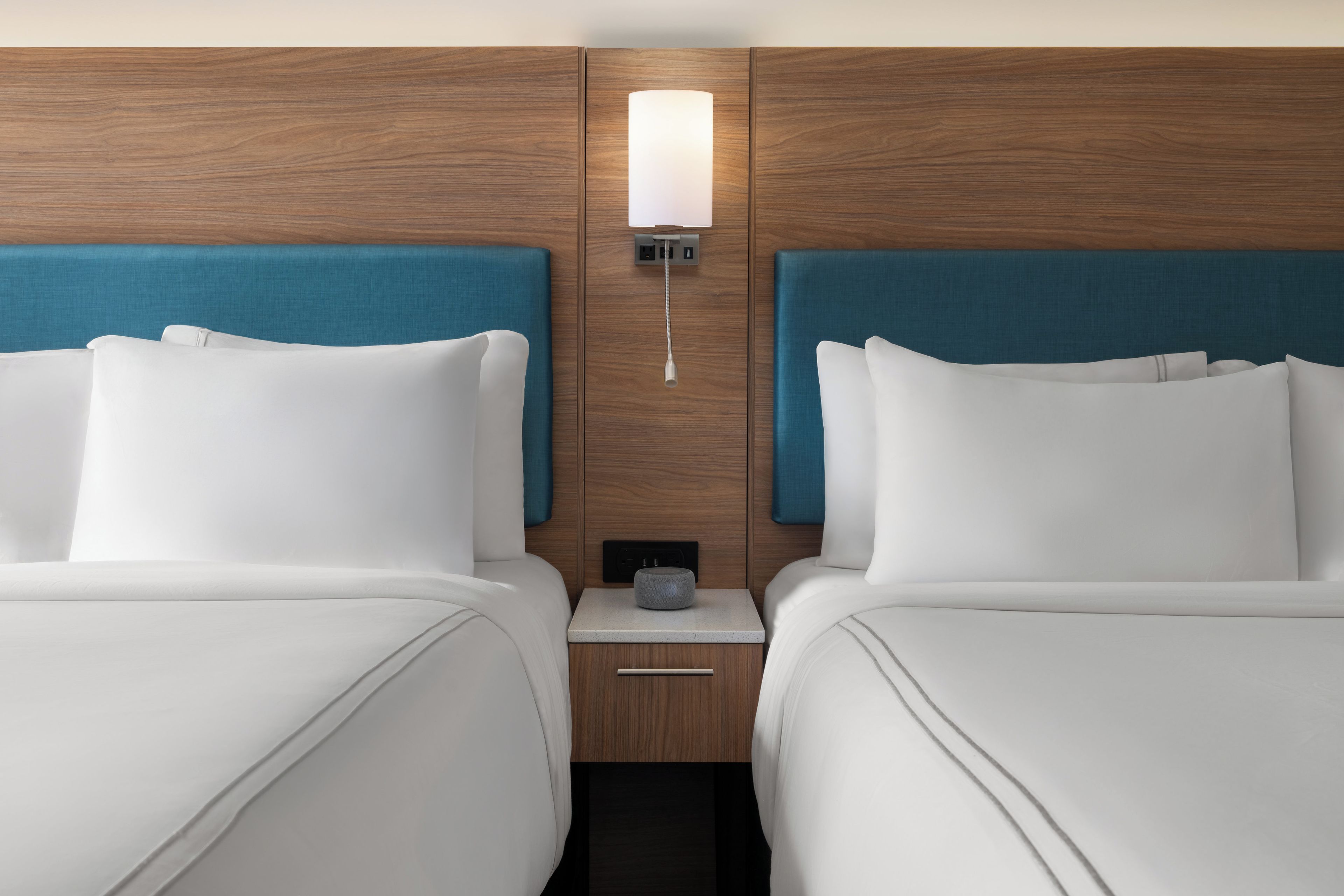 A hotel room with two beds, a nightstand, a lamp, and a power outlet.